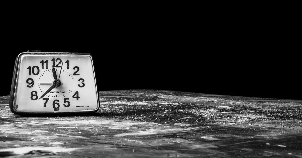 Di notte, una pila di schede che svaniscono una dopo l'altra davanti a un orologio fermo sulle tre e mezza, con una rete di sicurezza verde sotto che le raccoglie