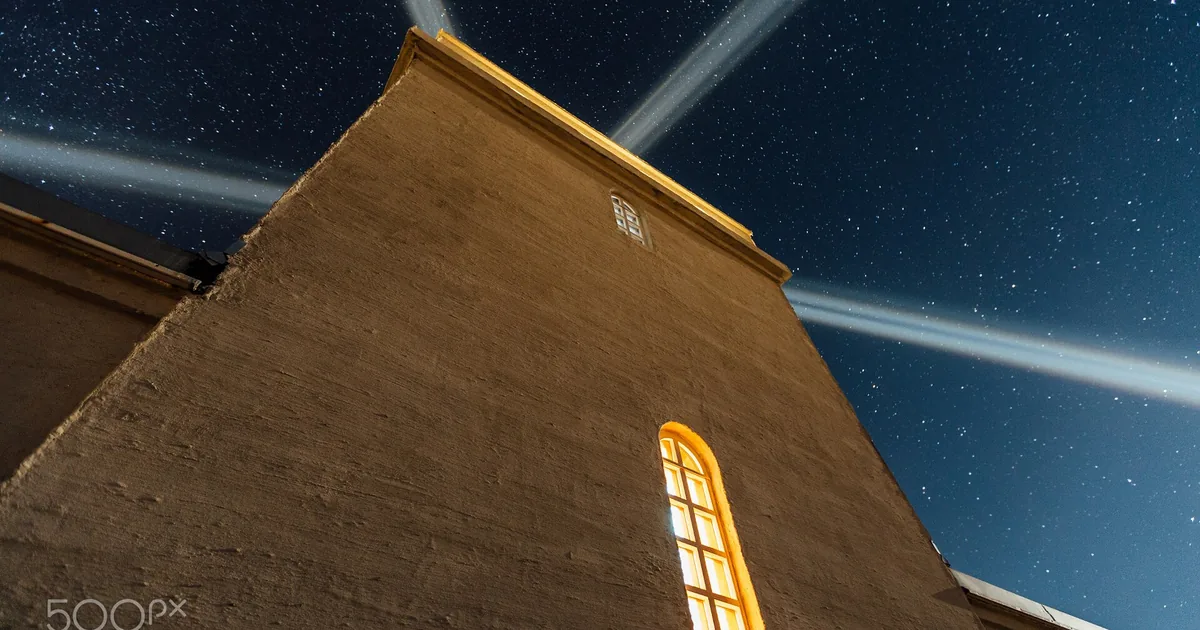 Una casa notturna con finestre accese collegata da linee di luce a una sua copia speculare sotto la luna