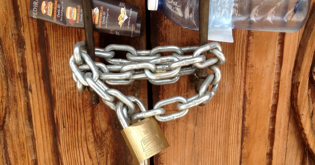 Una porta chiusa da un lucchetto accanto a uno scudo, con una sentinella a forma di occhio che veglia sotto una luna ambra