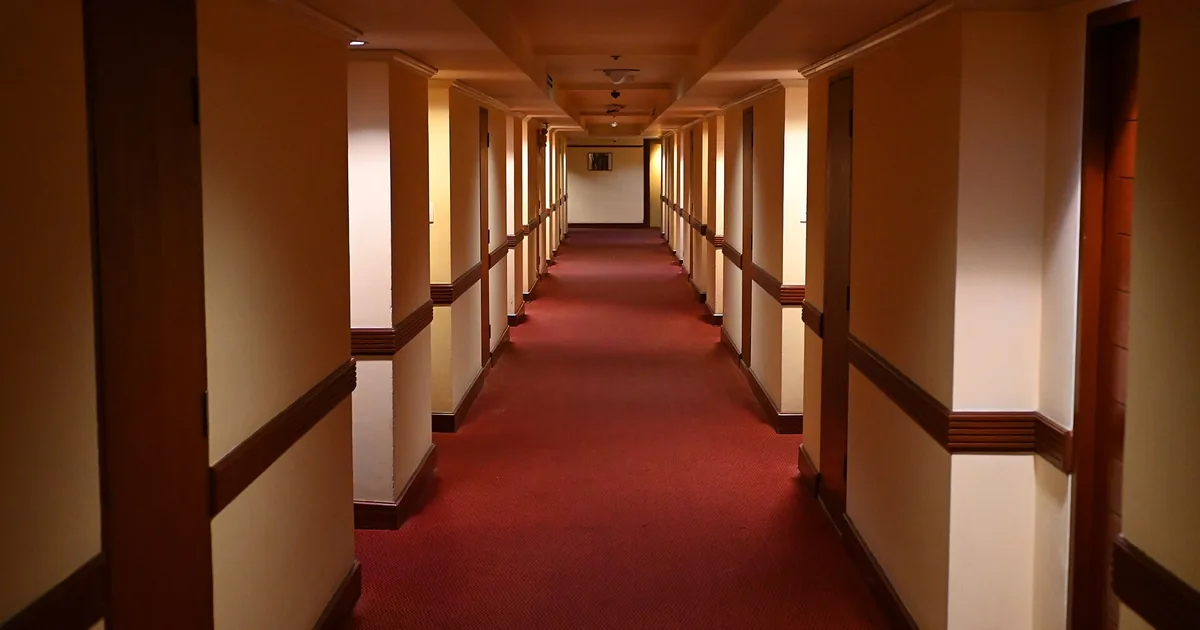 Una porta d'ingresso socchiusa in un corridoio buio, con una lama di luce calda che filtra dall'esterno
