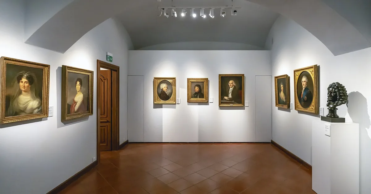 Una parete di cornici geometriche, una con un vuoto tratteggiato, accanto a una chiave ambra e a un piccolo orologio