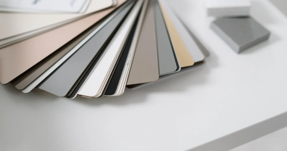 Una scrivania di notte con un monitor che mostra una pagina chiara e un cartoncino con campioni di grigio sotto la lampada