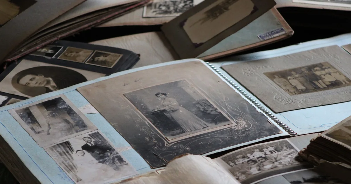 Una scrivania con un vecchio album di fotografie aperto accanto a un portatile acceso