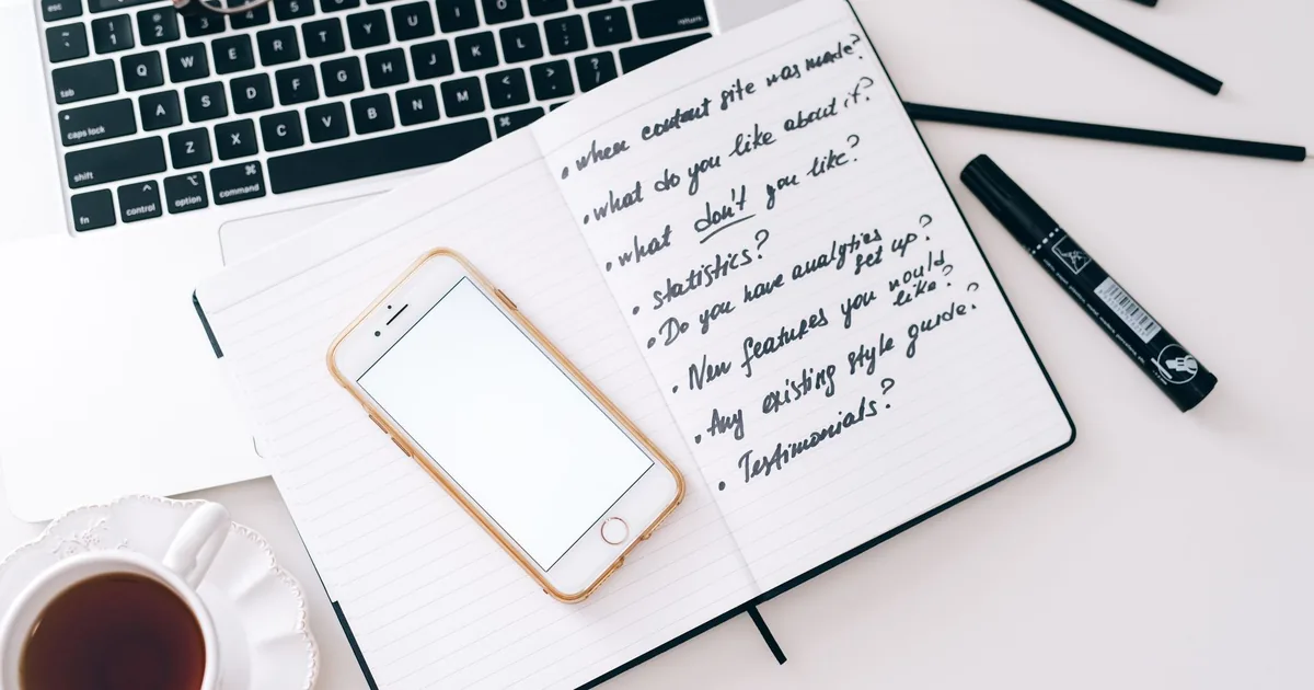 Uno smartphone acceso su una scrivania di notte, accanto a un quaderno di appunti e una tazza