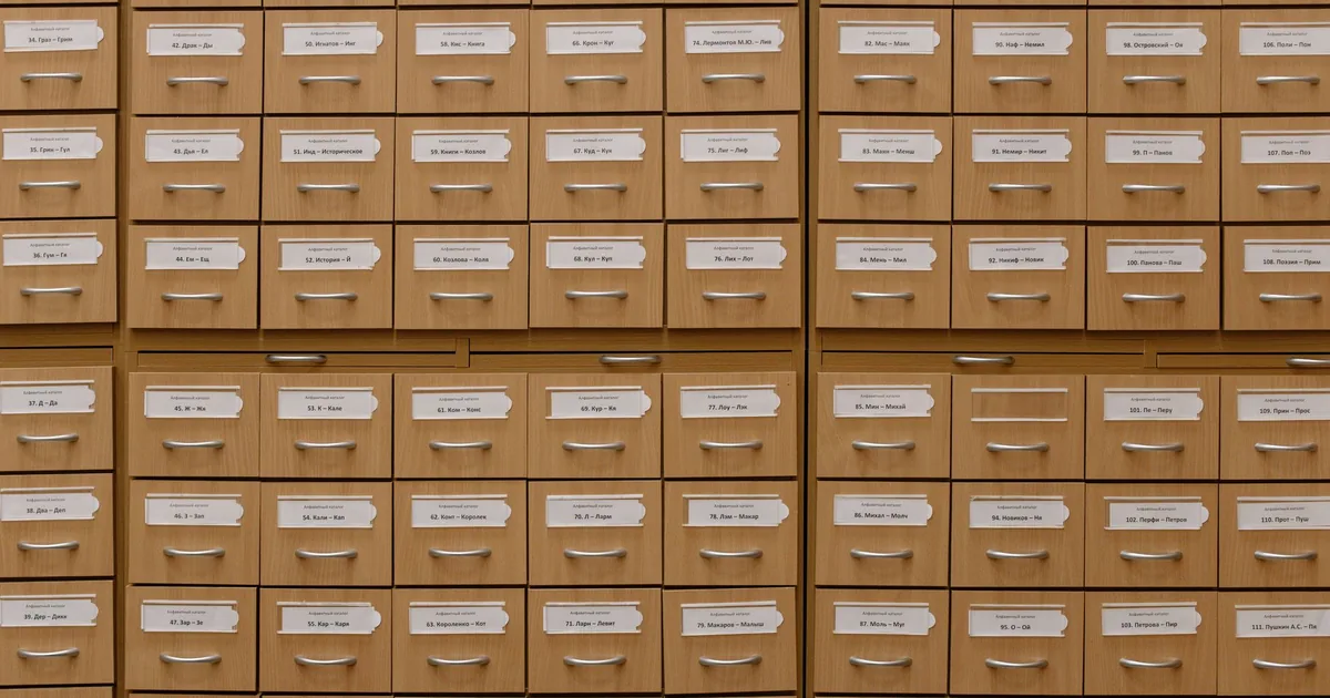 A wooden library card catalogue with one drawer pulled open, full of index cards