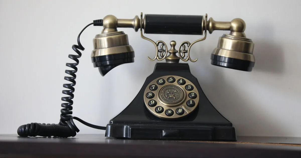 A telephone handset resting on a desk at night, lit by a lamp