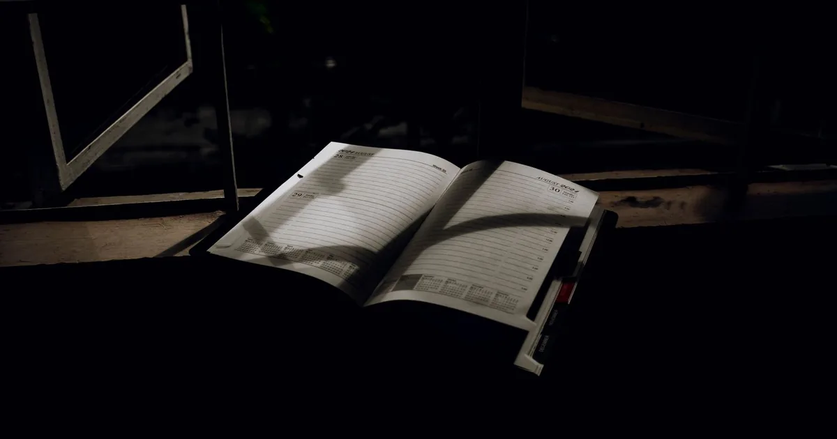 An empty wooden desk at dawn, with a single closed notebook and a cup